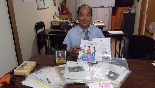 10年間分の奨学生写真と報告書を掲げる末松社長